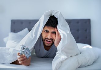 Arab man suffering from pain, lying in bed under blanket, waking up in the morning